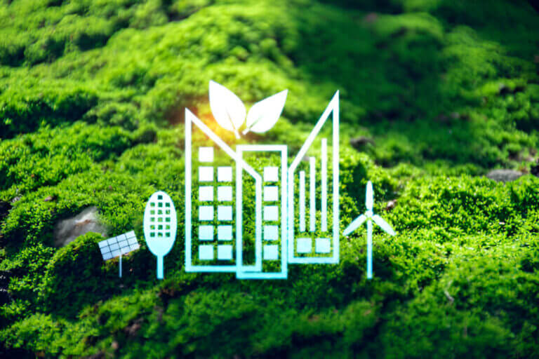 A 3D rendering depicting sustainable urban development. The image features icons such as a building with leaves, a solar panel, a wind turbine, and a tree-like structure, all set against a lush green moss background.